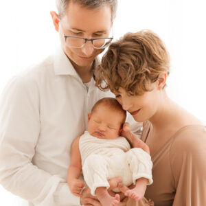 Eltern mit Baby am Arm vor weißem hellem Hintergrund