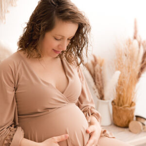 Schwangere hält ihren Bauch in braunem Kleid Boho Hintergrund