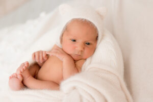 Babyfotos Neugeborenes in weißem Bettchen mit Bärenmütze