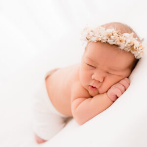 Baby liegt am Bauch auf weiß mit Blumenhaarkranz