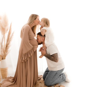 Schwangere küsst ihre Tochter und Papa küsst den Babybauch