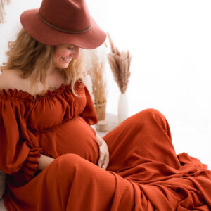 wunderschöne Schwangere in rotem Kleid mit Hut